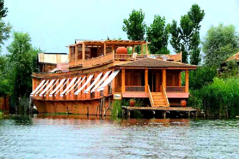 A traditional houseboat on Dal Lake, Srinagar, is surrounded by Himalayan mountains and peaceful Kashmir scenery.